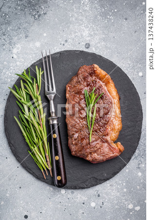 Close up of a flavorful grilled striploin or strip steak, garnished with herbs, ready to impress at your next dinner. grey background. top view Close up of a flavorful grilled striploin or strip steak, garnished with herbs, ready to impress at your next dinner. grey background. top view 137438240