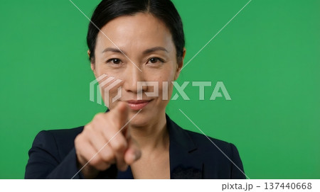 A professional Asian woman points directly at the camera against a green screen, suggesting direction or choice. 137440668