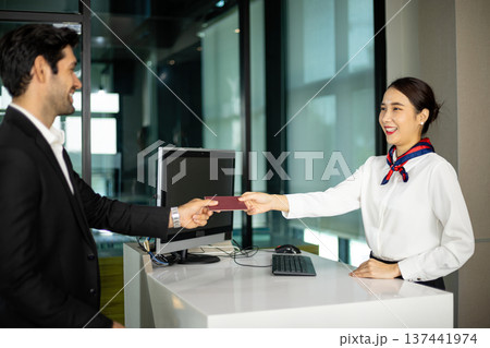 Airline female staff handing passport to passenger at counter during check in process. Friendly hospitality staff providing customer service and welcoming traveler Airline female staff handing passport to passenger at counter during check in process. Friendly hospitality staff providing customer service and welcoming traveler 137441974