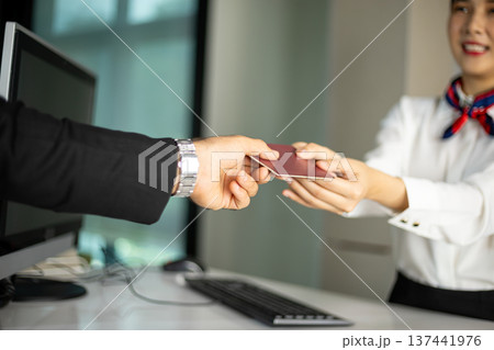 Airline female staff receiving passport from passenger at front desk during check in process. Close up hospitality service interaction 137441976