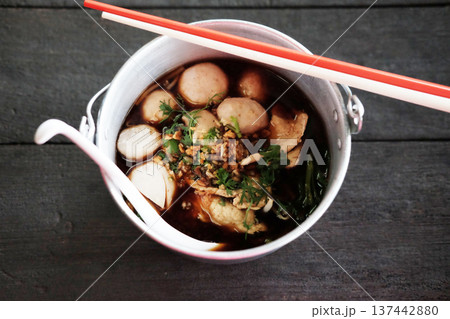 Top view of Thai boat noodles with chicken soup and pork balls in aluminum bowl on wooden table Top view of Thai boat noodles with chicken soup and pork balls in aluminum bowl on wooden table 137442880
