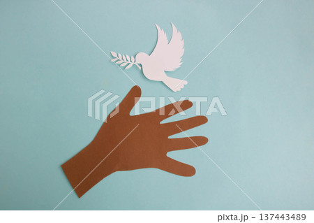 A paper hand reaches out to a paper dove on a blue background. World Peace Day. A paper hand reaches out to a paper dove on a blue background. World Peace Day. 137443489