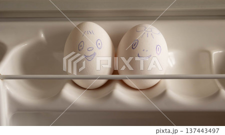 Two eggs with funny faces painted on them are on the refrigerator shelf Two eggs with funny faces painted on them are on the refrigerator shelf 137443497