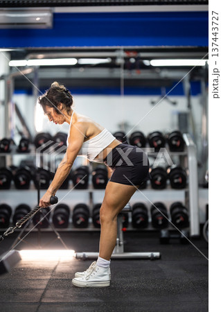 Woman training arm strength with cable machine in gym Woman training arm strength with cable machine in gym 137443727