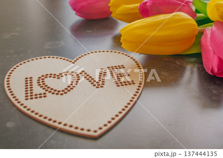 Dark moody composition of yellow and pink tulips on black marble with a wooden heart sign Love . High-contrast floral aesthetic for Mother's Day and spring branding Dark moody composition of yellow and pink tulips on black marble with a wooden heart sign Love . High-contrast floral aesthetic for Mother's Day and spring branding 137444135