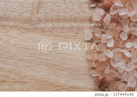 Coarse Himalayan pink salt crystals scattered on a natural wood surface. Tactile organic composition with warm timber grain, coral mineral tones, and copy space 137444149