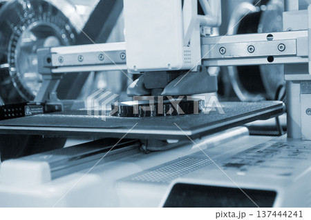 3D printer close up. Working 3D printer in process of printing object from molten black plastic. 3D printer creating model by flowing liquid plastic from extruder of printer. 3D printing technology 137444241