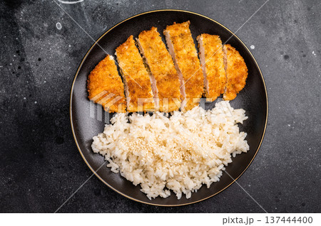 Delicious katsu style dish, featuring a perfectly cooked chicken meat cutlet served alongside steamed rice for a balanced meal. black background. top view 137444400