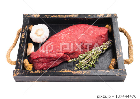 Raw beef topside on rustic wooden tray with thyme and garlic. Fresh lean inside round meat on isolated background with copy space. 137444470