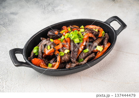 Beef stir fry with peppers and green onion cooked in skillet. Chinese pepper steak inspired beef strips dish on light background. Beef stir fry with peppers and green onion cooked in skillet. Chinese pepper steak inspired beef strips dish on light background. 137444479