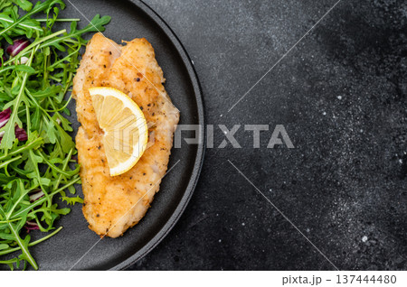 Pan fried red ocean perch fish fillet served with fresh arugula salad and lemon on dark background. Pan fried red ocean perch fish fillet served with fresh arugula salad and lemon on dark background. 137444480