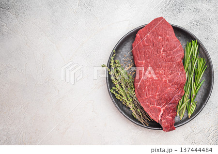 Fresh raw beef sirloin tip knuckle on dark ceramic plate. Lean butcher cut red meat prepared for cooking on light background. 137444484