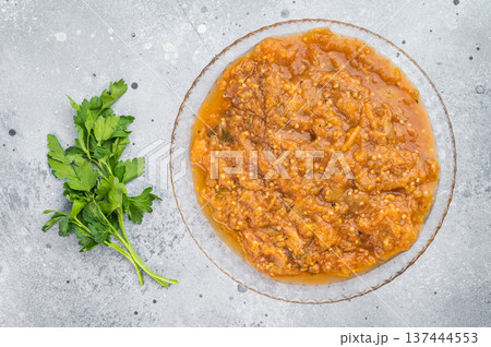 Traditional roasted eggplant dip melitzanosalata inspired vegetable relish presented in transparent plate overhead on light concrete background 137444553