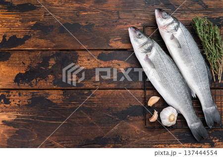 Two whole raw sea bass fish with thyme and garlic on rustic wooden background, fresh Mediterranean seafood ingredient for healthy gourmet cooking concept. Two whole raw sea bass fish with thyme and garlic on rustic wooden background, fresh Mediterranean seafood ingredient for healthy gourmet cooking concept. 137444554
