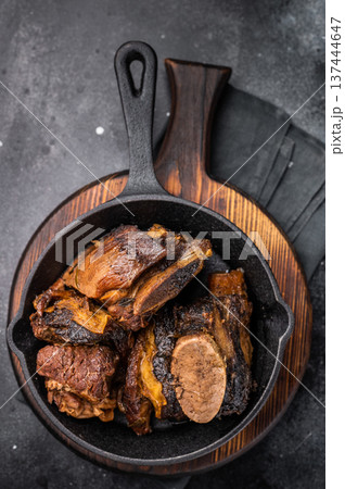Tender beef short ribs in a pan, seasoned with herbs and spices. Perfect for culinary blogs or restaurant menus that focus on hearty, flavorful meat dishes. black background. top view Tender beef short ribs in a pan, seasoned with herbs and spices. Perfect for culinary blogs or restaurant menus that focus on hearty, flavorful meat dishes. black background. top view 137444647