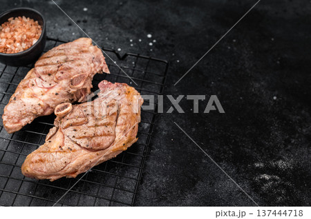 BBQ roasted lamb sirloin chops with bone placed on metal rack, seared surface with spices and pepper, gourmet grilled meat top view composition. BBQ roasted lamb sirloin chops with bone placed on metal rack, seared surface with spices and pepper, gourmet grilled meat top view composition. 137444718