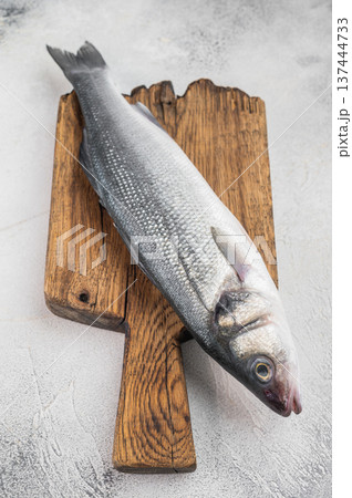 Fresh whole sea bass with thyme and garlic on rustic wooden board over isolated background, Mediterranean seafood ingredient with wide copy space. 137444733