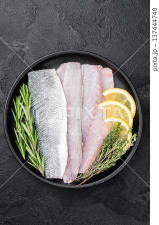 Uncooked European sea bass fillet on black plate with rosemary and thyme, clean culinary layout ideal for seafood menu, cooking recipe or nutrition design. Uncooked European sea bass fillet on black plate with rosemary and thyme, clean culinary layout ideal for seafood menu, cooking recipe or nutrition design. 137444740