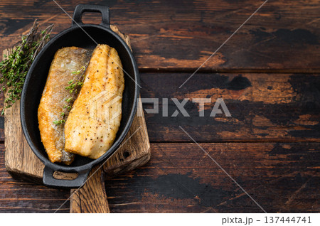 Crispy fried sea bass fish fillet with thyme in cast iron pan, mediterranean seafood dinner composition with rustic wooden background and copy space. 137444741