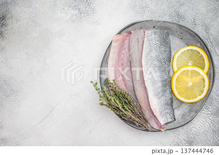 Raw sea bass fillet with skin served on plate with lemon and thyme, fresh Mediterranean seafood ingredient in minimal overhead food styling composition. 137444746