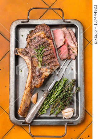 BBQ cooked Tomahawk beef steak, prime ribeye with bone on tray with herbs. dark background. top view BBQ cooked Tomahawk beef steak, prime ribeye with bone on tray with herbs. dark background. top view 137444923