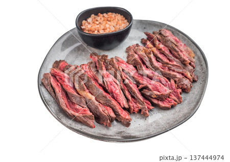 Sliced grilled machete skirt steak served with coarse salt on ceramic plate isolated 137444974