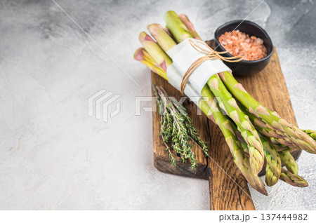 Green asparagus on wooden cutting board with herbs and salt, healthy vegetarian ingredient shot in minimal bright culinary style 137444982