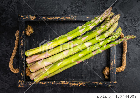 Raw asparagus bundle with rosemary and thyme on black tray, minimal dark food styling with vintage fork and culinary copy space. Raw asparagus bundle with rosemary and thyme on black tray, minimal dark food styling with vintage fork and culinary copy space. 137444988