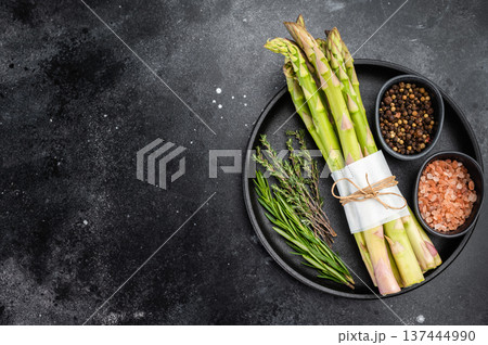 Fresh green asparagus bundle with rosemary, thyme and spices on black plate, dark rustic background with copy space, organic vegan ingredient concept 137444990