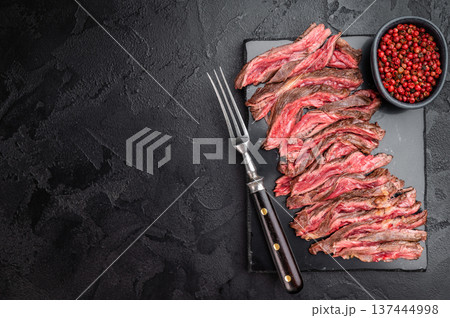 Grilled bavette flap steak sliced medium rare also known as arrachera machete or skirt steak served on dark slate with fork and red peppercorns rustic overhead food background 137444998