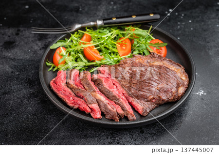 Grilled hanger onglet steak sliced and served with fresh arugula salad and cherry tomatoes on dark stone background top view Grilled hanger onglet steak sliced and served with fresh arugula salad and cherry tomatoes on dark stone background top view 137445007