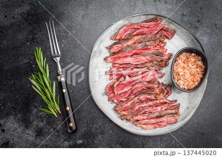 Grilled beef skirt steak slices with sea salt on ceramic plate rustic restaurant style presentation with copy space on dark surface 137445020