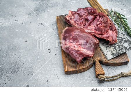 Whole and cut pork hearts highlighting anatomy muscle fibers and valves with garlic thyme and chopping cleaver nearby. Whole and cut pork hearts highlighting anatomy muscle fibers and valves with garlic thyme and chopping cleaver nearby. 137445095