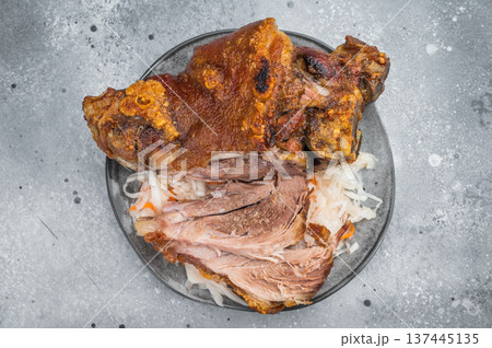 Crispy roasted pork knuckle with sliced tender shank meat served on sauerkraut over gray stone background with mustard and fork styling. Crispy roasted pork knuckle with sliced tender shank meat served on sauerkraut over gray stone background with mustard and fork styling. 137445135