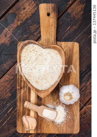 Dried granulated garlic seasoning with fine texture in wooden bowl. Rustic culinary ingredient flatlay background. Dried granulated garlic seasoning with fine texture in wooden bowl. Rustic culinary ingredient flatlay background. 137445136