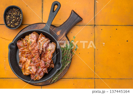 Crispy sizzling bacon in castiron skillet on warm yellow tile background creating bold contrast and appetizing gourmet mood. 137445164