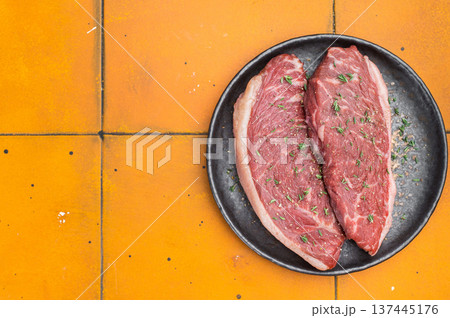 Raw beef culotte steaks also called picanha or rump cap on black ceramic plate, bright yellow stone background 137445176