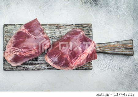 Raw lamb and goat hearts on rustic cutting board with visible muscle fibers fascia and natural texture beside rosemary and pepper. 137445215