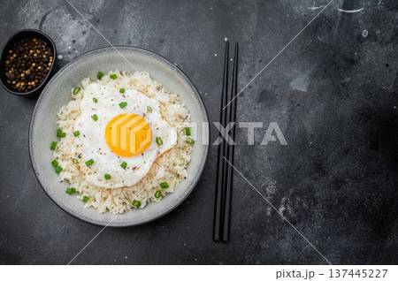 Soft rice and crisp edged fried egg in a rustic bowl photographed on dark textured background for modern culinary content. 137445227