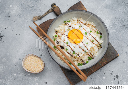 Fried egg with glossy yolk over fluffy rice and sweet glaze offering a clean Asian fusion dish perfect for contemporary food styling. 137445264