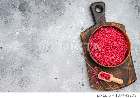 Freeze dried raspberry granules in wooden bowl with spoon on board. Vibrant berry ingredient flatlay with copy space 137445275