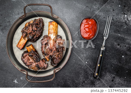 Cooked beef ribs slow cooked until tender with bone and sauce. BBQ style beef plate ribs on dark stone background with copy space. 137445292