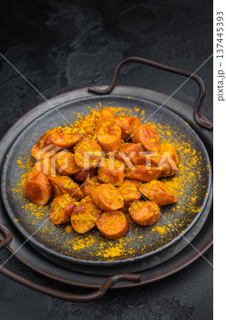 German currywurst, sausages with curry spice served on rustic metal plate over dark textured background perfect for street food and stock imagery. German currywurst, sausages with curry spice served on rustic metal plate over dark textured background perfect for street food and stock imagery. 137445393