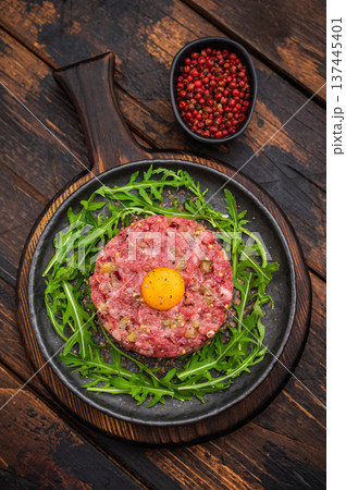 Raw beef tartare with egg yolk and arugula on wooden surface great for gourmet cooking protein rich meals and high quality food photography. Raw beef tartare with egg yolk and arugula on wooden surface great for gourmet cooking protein rich meals and high quality food photography. 137445401