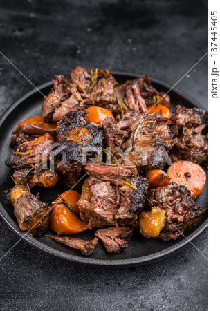 Slow cooked oxtails with vegetables and herbs, hearty comfort food served on dark background, top view Slow cooked oxtails with vegetables and herbs, hearty comfort food served on dark background, top view 137445405