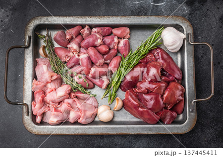 Raw duck liver, hearts, and gizzards on metal tray with garlic and rosemary on dark textured background, fresh poultry offal. Raw duck liver, hearts, and gizzards on metal tray with garlic and rosemary on dark textured background, fresh poultry offal. 137445411