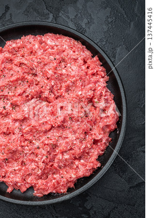 Fresh raw ground mince beef and pork meat with seasoning on black plate over dark textured background ideal for cooking, butcher and protein ingredient themes. Fresh raw ground mince beef and pork meat with seasoning on black plate over dark textured background ideal for cooking, butcher and protein ingredient themes. 137445416