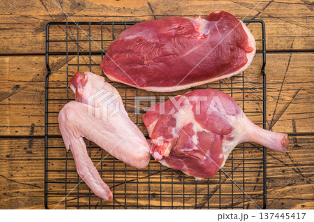 Fresh uncooked duck cuts breast fillet thigh and wingarranged on cooling grid against scratched wood surface perfect for culinary preparation visuals. Fresh uncooked duck cuts breast fillet thigh and wingarranged on cooling grid against scratched wood surface perfect for culinary preparation visuals. 137445417