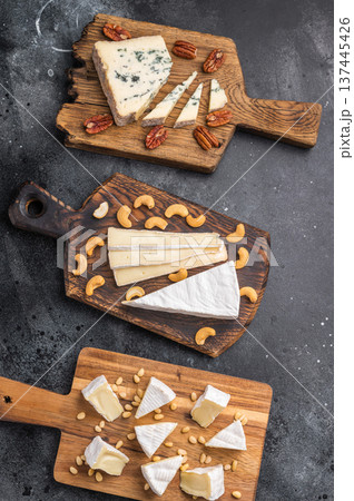 Brie Camembert and Roquefort served on rustic wooden boards with mixed nuts placed over a dark artistic background. 137445426