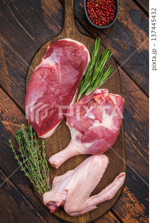 Plucked raw duck meat selection displayed on rustic board with seasoning against dark wood backdrop showcasing premium poultry. 137445432